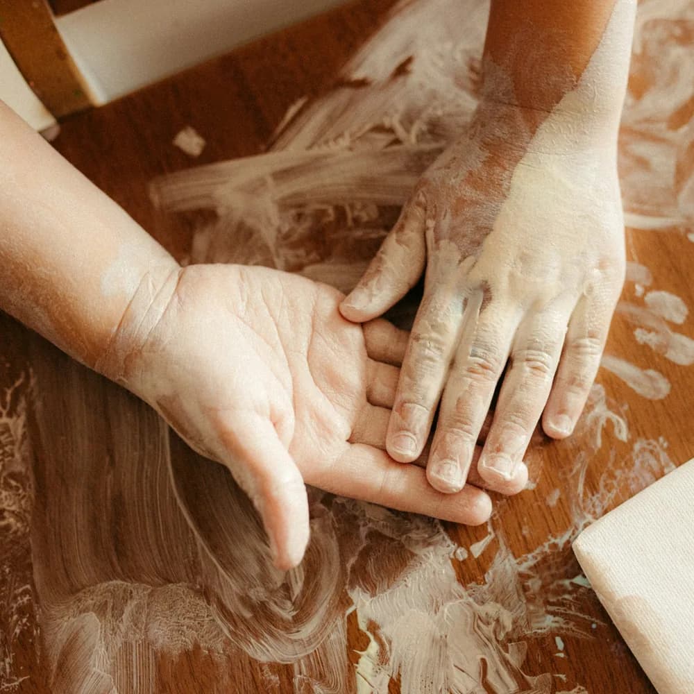 An adult's and a child's hands working together in flour on a wooden board
